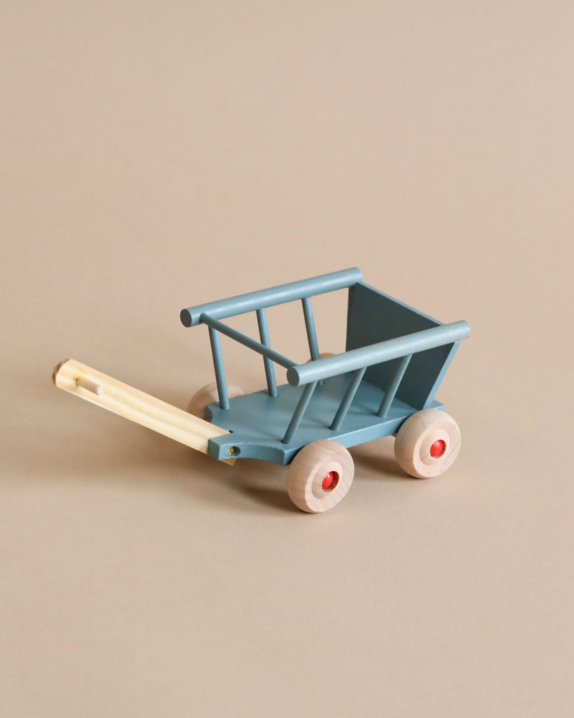 A Maileg Wagon, characterized by a minimalist design and constructed primarily from smooth, painted wood, is placed against a neutral background. This small blue wooden wagon features four beige wheels and a matching beige handle, making it perfect for carrying groceries.