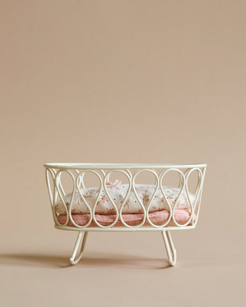 A white wire rack holding four Maileg Miniature Cradles with pink sand on a beige background, suggesting a minimalist and elegant design.