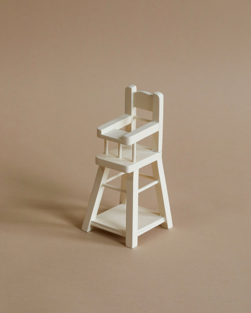 A Maileg Micro High Chair with a simple ladder-back design is placed on a neutral beige background. The chair features armrests and a footrest, and is neatly crafted with clean lines and a minimalistic aesthetic—perfect for micro bunnies and rabbits or micro-sized Maileg friends.