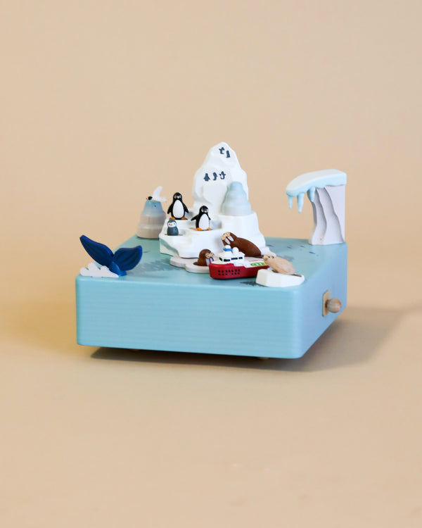 A Wooden Antarctica Music Box from Wooderful Life, featuring a polar bear with sunglasses, a fish tail, penguin, and other small details crafted from sustainably sourced wood, set against a miniature beach scene diorama.