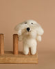 The Maltese Dog Finger Puppet sits gracefully on a wooden stand, showcasing its intricate, handmade detail and charming character.