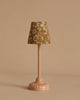 Introducing the Maileg Royal Tea Party lamp: a charming, small furnished table lamp featuring a pink base and a floral-patterned lampshade perfect for any Tea Party setting. The shade showcases white flowers on mustard fabric set against a neutral beige backdrop, adding an enchanting touch to any room.