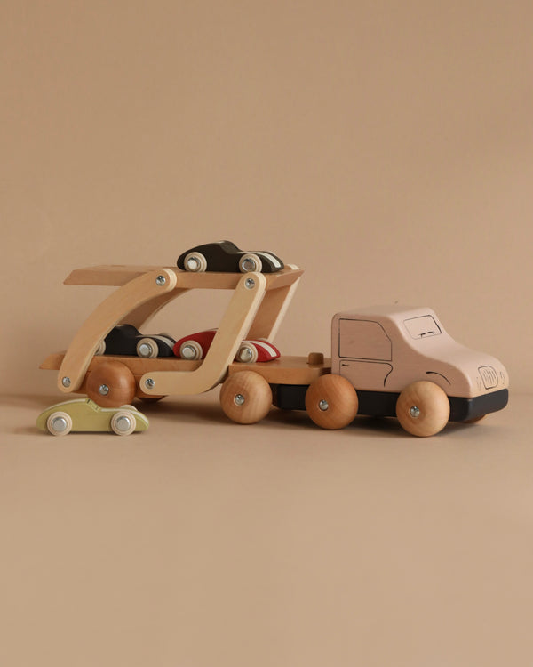 The Konges Sløjd - Wooden Car Transporter is a delightful set featuring a wooden truck and car carrier, complete with small race cars, all made from FSC-certified beech wood. The minimalist designs in natural wood tones contrast beautifully against a neutral beige backdrop, providing timeless playtime enjoyment.