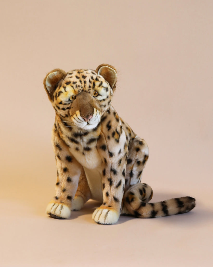 The Leopard Cub Stuffed Animal is positioned against a neutral beige background. Hand sewn with detailed spots, a long tail, and soft fur texture, it features realistic qualities that give it a lifelike appearance.