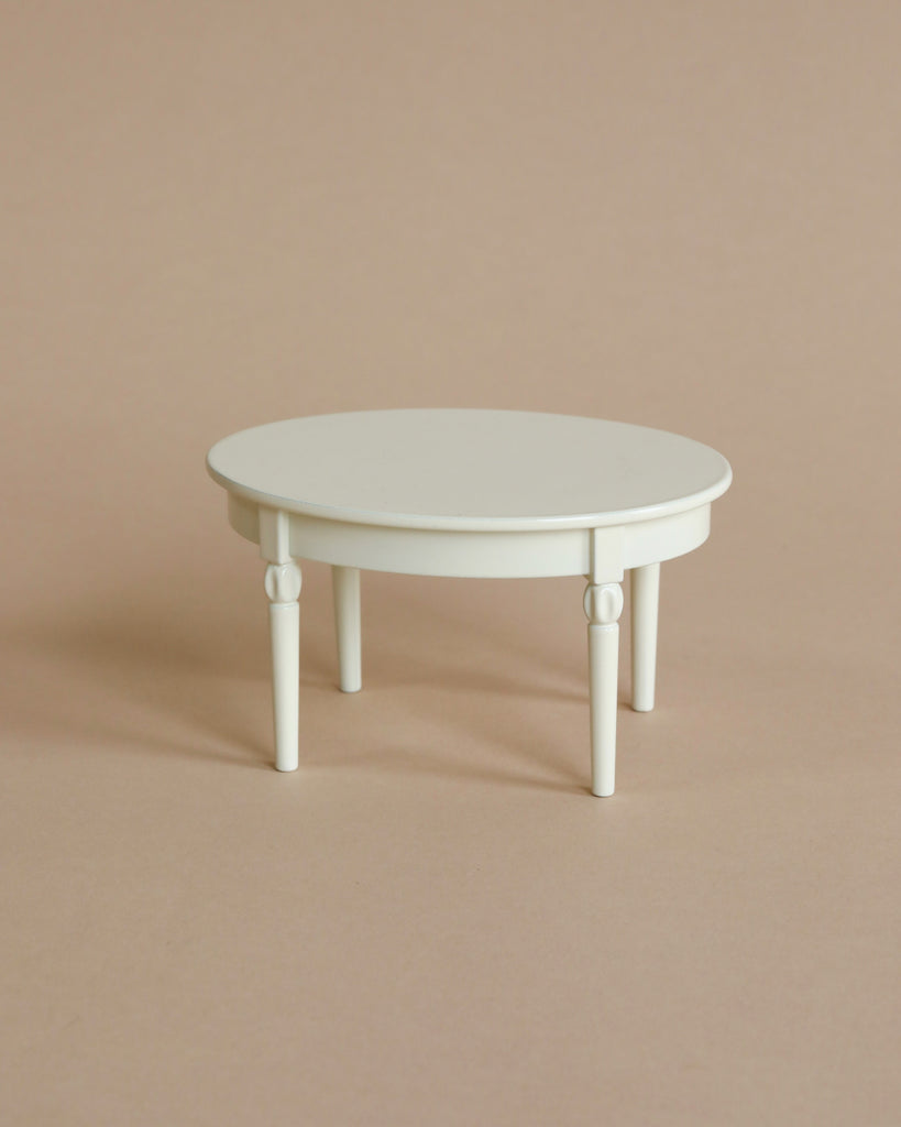 A simple, small, white circular Maileg Miniature Dining Table with four legs, set against a plain light beige background.