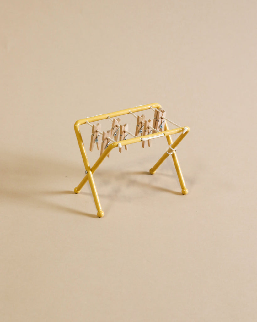 A small, yellow Maileg Drying Rack, Mouse Size with small wooden pegs attached to its bars is positioned against a plain beige background. The drying rack is empty, with no clothing or items hanging on it.