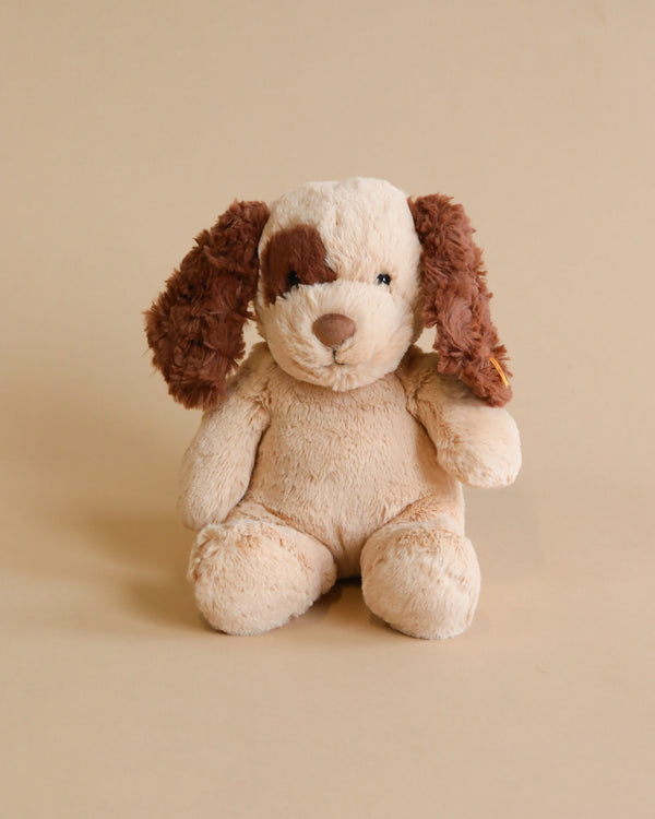 A Steiff Peppi Puppy Dog, 11 Inches plush toy with brown ears and a cream-colored body sits facing the camera against a plain light beige background.