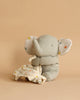 A Maileg Lullaby Friends - Elephant - Iron grey (Plays Music) with large ears sits on a beige background. The baby toy has its trunk wrapped around a soft, white blanket adorned with colorful polka dots. The overall atmosphere is cozy and gentle, perfect for playing Mozart's lullaby in a nursery.