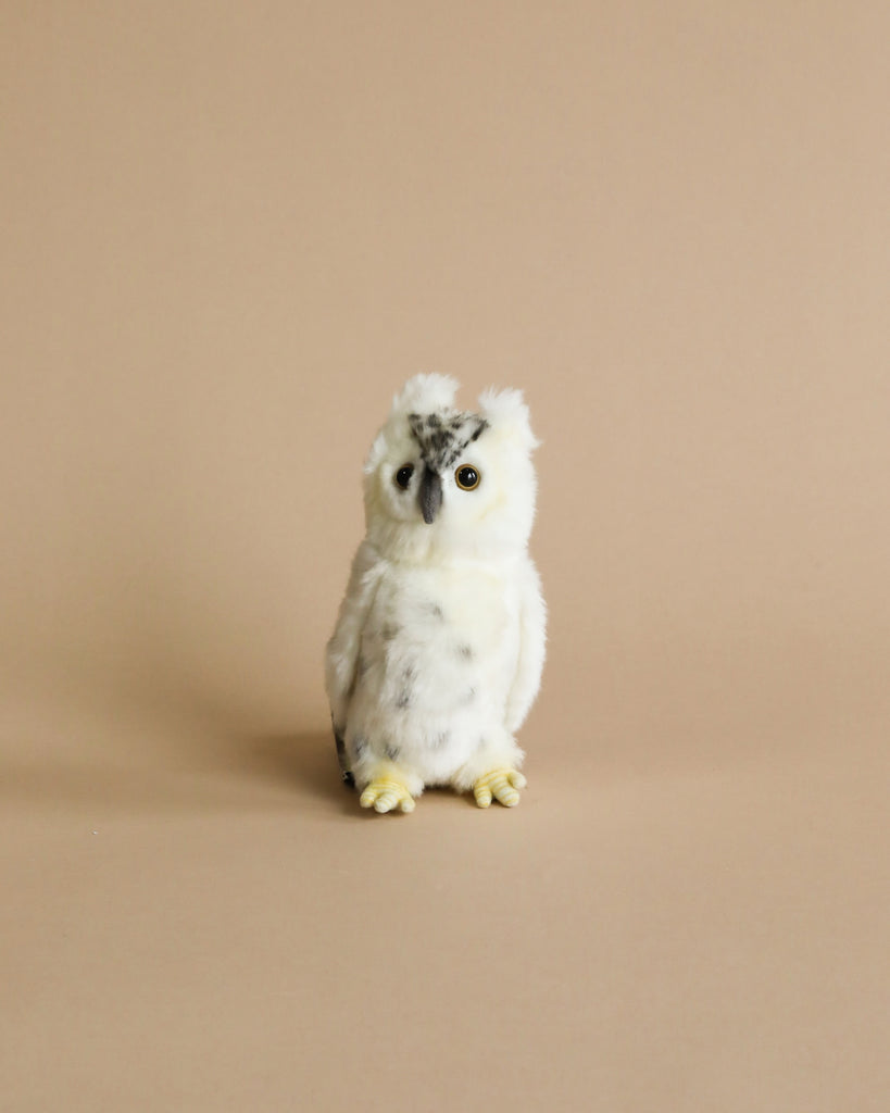 A Small White Owl Stuffed Animal, crafted from high-quality materials, with distinctive tufts of feathers resembling eyebrows perches against a soft beige background, looking directly at the camera with bright yellow eyes.