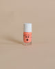 A small bottle of peach-colored Nailmatic washable nail polish with a cute face drawn on it, featuring eyes, eyebrows, and lips, set against a plain beige background.