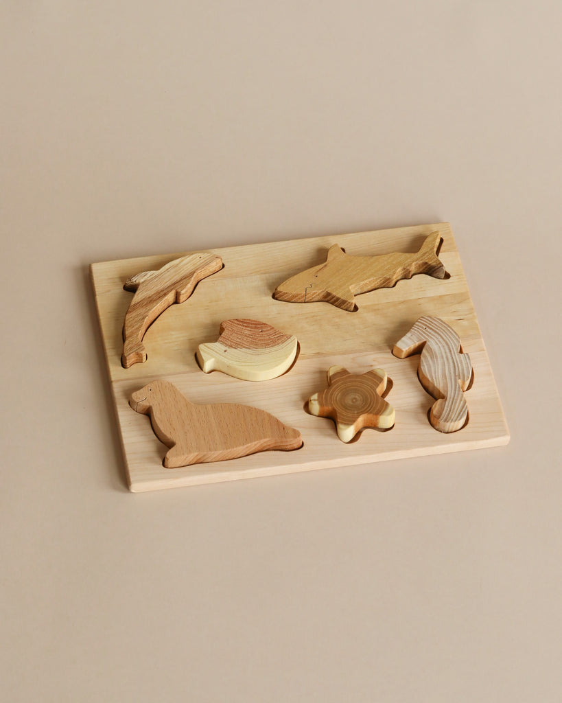 A Handmade Wooden Ocean Puzzle featuring sea animals, including a dolphin, whale, shark, sea horse, turtle, and sea lion. Each piece is made from different kinds of wood and treated with linseed oil and beeswax. The pieces are beautifully arranged on a light-colored wooden board against a beige background.