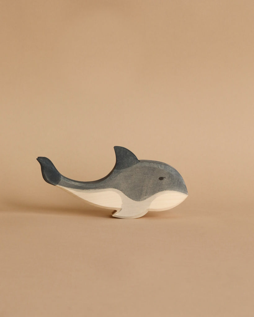 An Ostheimer Whale is placed against a beige background. The whale, with blue-grey and white coloring, has a simple, smooth design featuring a prominent dorsal fin, a curved tail fin, and a small eye—perfect for imaginative play.