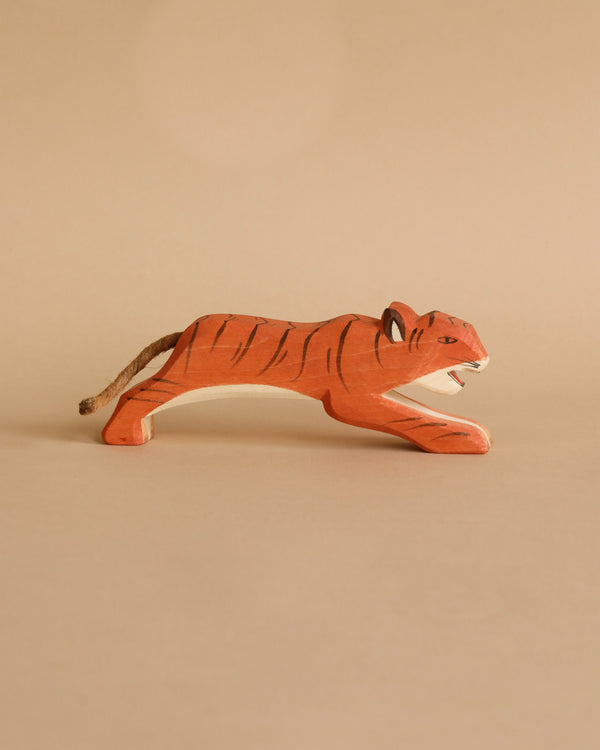 A wooden Ostheimer Jumping Tiger painted in orange with black stripes is shown against a beige background. The tiger, perfect for imaginative play, is in a prowling position with an open mouth and features a rope tail. Handcrafted with care, this piece embodies the quality of Ostheimer toys.