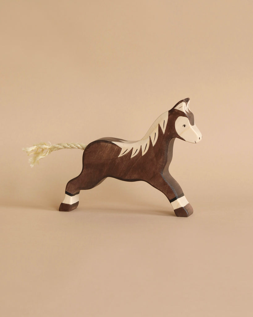 A Holztiger Horse, Running, Dark Brown toy, handcrafted out of wood, is depicted against a plain background. The horse is painted in dark brown and white, standing in a prancing position with a string tail. Made in Europe, the toy's simple and charming design captures a sense of playful nostalgia reminiscent of HOLZTIGER figures.