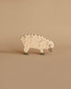 A small wooden toy resembling a sheep, handcrafted wood and painted beige with darker curved lines representing wool texture. The high-quality Holztiger Sheep, Eating stands on a neutral beige background, and its simple design includes a gray snout and feet, reminiscent of HOLZTIGER figures.