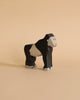 A Holztiger Gorilla is standing on a beige surface against a beige background. Made in Europe from handcrafted wood, the gorilla is painted in black and light grey with simple facial features and details, showcasing a minimalist design.