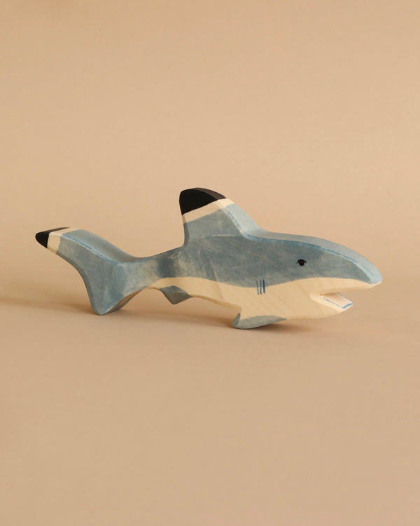 A handcrafted Holztiger Shark with blue and white painted sections and a small black fin, placed against a plain beige background. The shark has simple, minimalist design details, embodying the high-quality, playful aesthetic characteristic of HOLZTIGER figures.