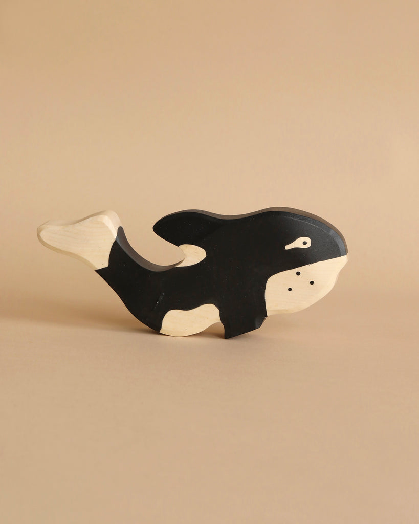 A handcrafted Holztiger Orca Whale with a black and white body is placed against a plain beige background. The orca, part of the HOLZTIGER figures collection, is simplistic in design with smooth edges and minimal detailing, showcasing the meticulous craftsmanship made in Europe.