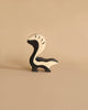 A minimalist Holztiger Skunk, reminiscent of HOLZTIGER figures, stands on a plain beige background with a black and white color palette. Its tail is prominently arched over its back, showcasing the simple yet abstract design. Made in Europe from handcrafted wood.