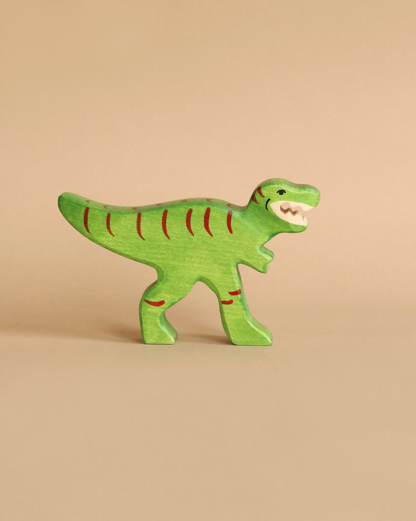 A small, green wooden Holztiger Tyrannosaurus Rex Dinosaur with red stripes and an open-mouthed expression is standing on a beige background. Handcrafted wood gives it a simplified, cartoonish design, reminiscent of HOLZTIGER figures and proudly made in Europe.