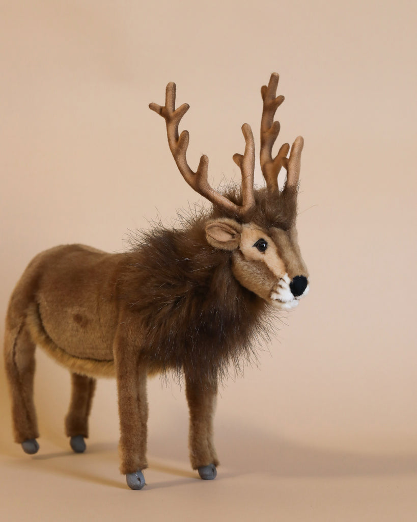 Set against a simple beige backdrop, the Brown Reindeer Stuffed Animal, measuring 15 inches, is a hand-sewn plush toy featuring multiple antlers. It boasts a brown body with a fluffy mane and small gray hooves, designed to exhibit realistic details.