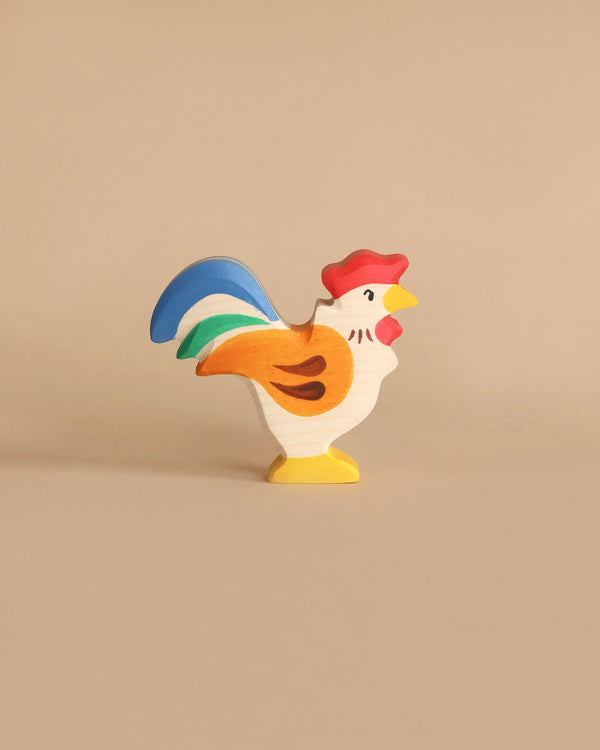 A Holztiger Rooster, made in Europe and painted in bright colors, features a red comb, yellow beak, white body with orange feathers, and a blue and green tail. This handcrafted wood piece stands upright on a neutral tan background and epitomizes the charm of HOLZTIGER figures.