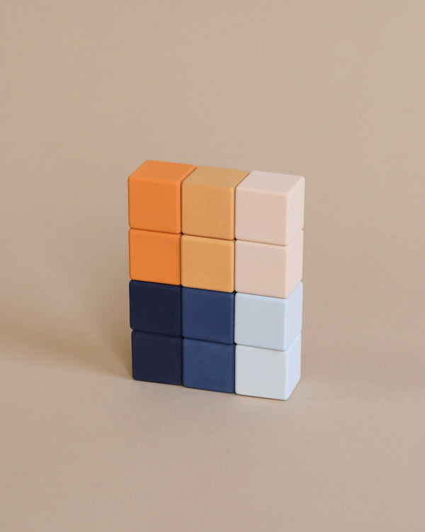 A neatly stacked 3x3 grid of colorful Mini Wooden Blocks - Desert Night handcrafted by Sabo Concept against a plain beige background. The handmade stacking toy features non-toxic paint in vibrant hues, including orange, beige, light pink, dark blue, and light blue.