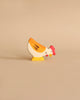 A small, colorful wooden figurine of a hen stands on a plain beige background. Handcrafted out of maple and beech wood, this Holztiger Hen, Pecking figure is painted with yellow, white, and orange body parts and has a red comb on its head. The simple, cartoonish design adds a playful touch to the figurine.