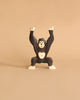 A wooden toy chimpanzee with outstretched arms stands on a plain beige background. Handcrafted from maple and beech wood, this Holztiger Chimpanzee, Standing figure is designed with simplified features and painted in dark brown with white accents on its hands, feet, and face.