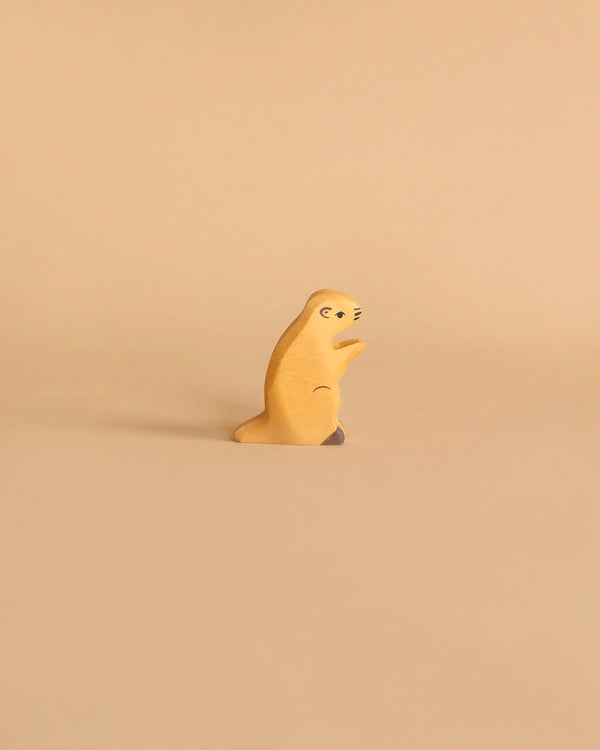 A small handcrafted wooden figure of a meerkat stands upright against a light beige background. The Holztiger Groundhog is crafted simply, with minimal details to represent the meerkat's eyes, nose, and limbs. Made in Europe, it exudes charm and simplicity.