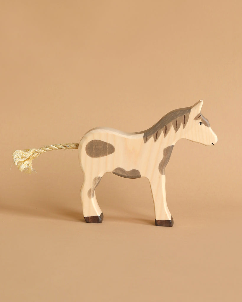 A Holztiger wooden horse figure from Noah's Ark with Animals features a simple design and brown patches on a beige surface, its braided tail adding charm. The matching background enhances the natural tones of this solid wood toy.