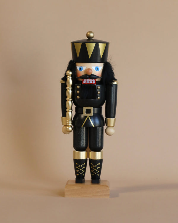 The Christian Ulbricht Collectible Wooden Nutcracker - King In Black is a limited-edition traditional German nutcracker, painted in black and gold. It features blue eyes, a black hat with gold trim, and holds a golden staff while standing upright on a wooden base against a plain beige background.