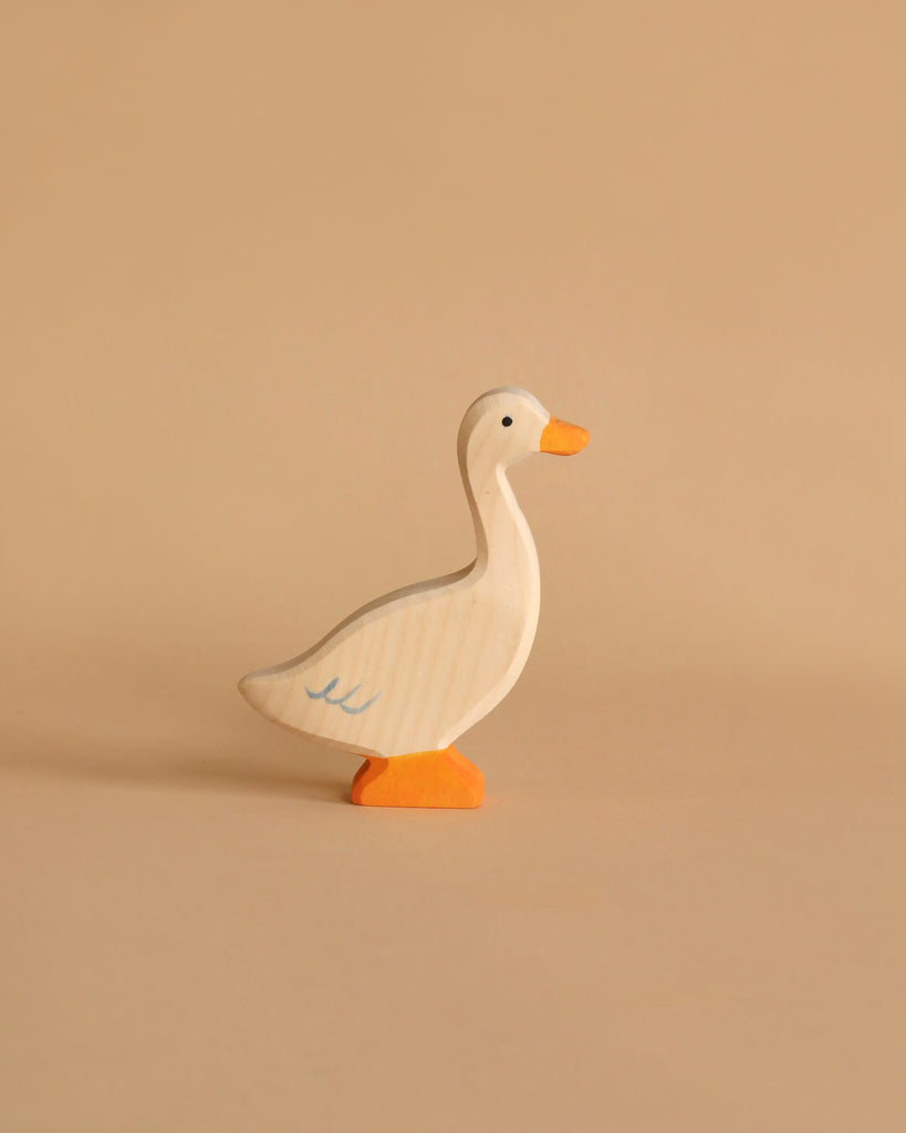 A small wooden goose figurine stands on a plain beige background. The goose, reminiscent of Holztiger Goose, Standing figures, is white with subtle gray accents and features an orange beak and feet. It appears to be handcrafted wood with a simple, minimalist design that exudes timeless charm.