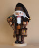 The Christian Ulbricht Collectible Wooden Nutcracker, known as the Natural Woodsy Santa With Lantern, is a limited-edition creation dressed in a brown and green plaid coat and hat. This nutcracker holds a wooden lantern and pine cones, has a white beard and round glasses, and stands proudly on a wooden base set against a beige background.