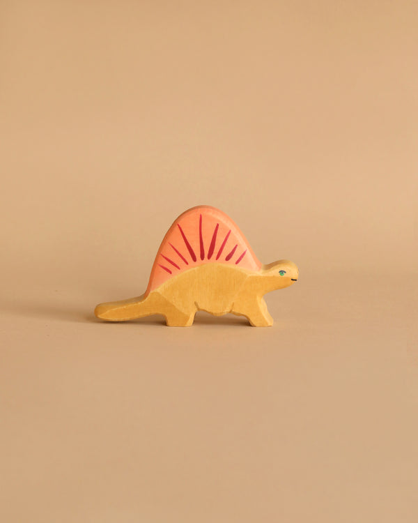 A Holztiger Dimetrodon Dinosaur with a yellow body and a pink, fin-like structure on its back stands against a light beige background. This handcrafted wood figure features a simple design, painted eyes, and minimal detailing, reminiscent of the charming HOLZTIGER figures made in Europe.