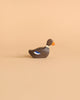 A small wooden Holztiger Swimming Duck with a dark brown body, a white stripe around its neck, an orange beak, and a small blue detail on its side. Handcrafted with care like HOLZTIGER figures, the high-quality duck is positioned facing right on a light brown background.