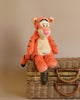 The Steiff Disney's Tigger the Tiger Stuffed Plush Toy, measuring 12 inches and showcasing an orange tiger with black stripes and a pink nose, is charmingly displayed on a wicker suitcase against a light brown background.