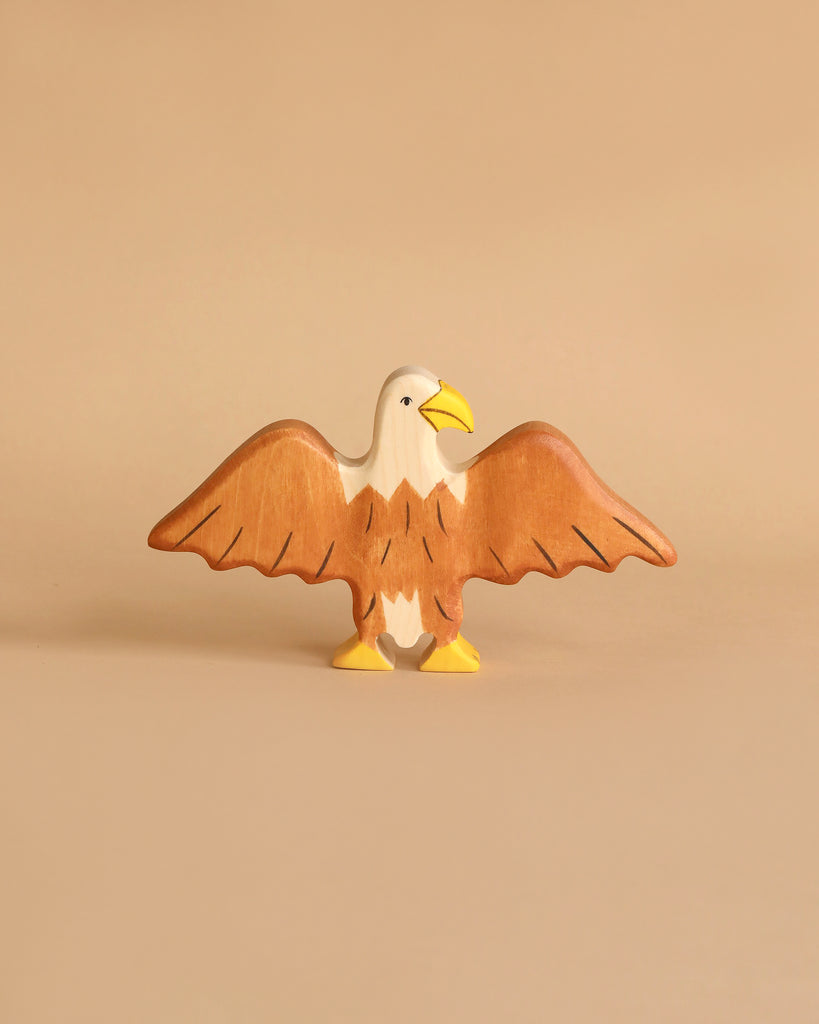 A small, individually handcrafted wooden figurine of a bird with outstretched wings. Made from durable maple and beech wood, the Holztiger Eagle has a white head, a yellow beak, and brown body and wings, presented against a beige background. A charming addition to any HOLZTIGER figures collection.