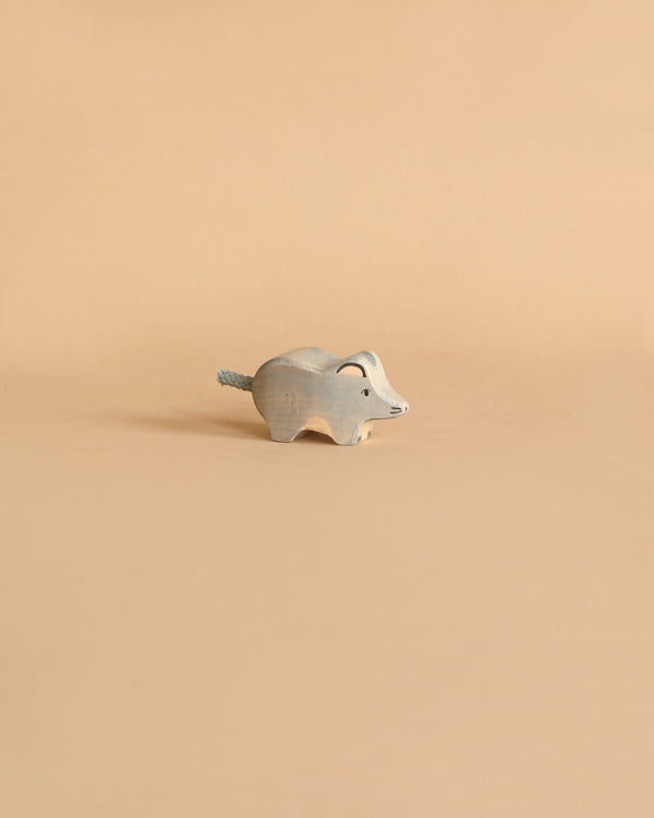 A small, wooden, hand-carved figurine of an elephant is placed against a plain beige background. Handcrafted out of maple and beech wood with a minimalist design in light blue-gray, its tail is accented with a piece of string, reminiscent of the charming Holztiger Mouse.