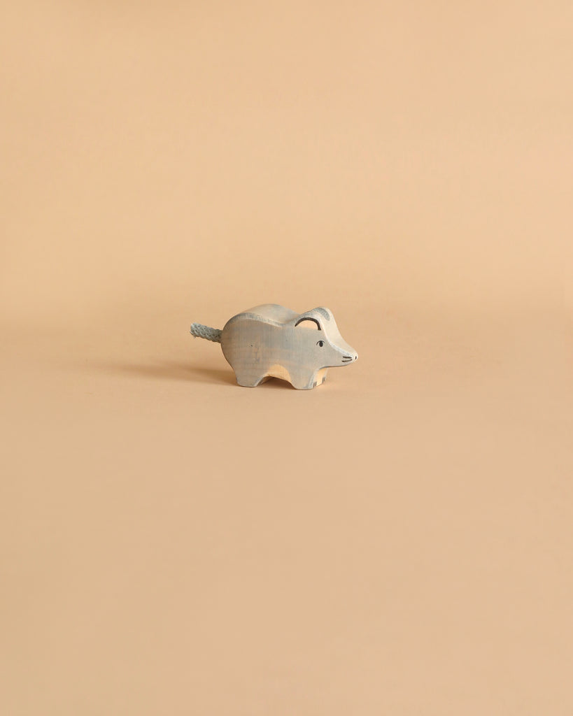 A small, wooden, hand-carved figurine of an elephant is placed against a plain beige background. Handcrafted out of maple and beech wood with a minimalist design in light blue-gray, its tail is accented with a piece of string, reminiscent of the charming Holztiger Mouse.