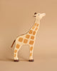 A Holztiger Giraffe, Head Raised, handcrafted from wood, stands against a plain beige background. Made in Europe by HOLZTIGER figures, the giraffe has a light brown body with darker brown spots, short legs, and a small tail. Its head is raised and tilted slightly upwards.