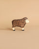 A small, brown Holztiger Brown Sheep, Standing figurine with a woolly texture is shown against a plain beige background. The handcrafted wood sheep has detailed carvings to represent its wool and black hoofs. Made in Europe.