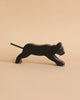 A small, sleek black Holztiger Panther with a minimalist design is shown in a side view, appearing to be in a poised, walking stance. Handcrafted from wood and part of the renowned HOLZTIGER figures, it exudes simple elegance against the plain light beige background. Made in Europe.