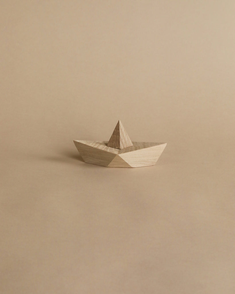 Sentence with Product Name: A Boyhood Admiral, Small Oak origami-style boat on a plain beige background, featuring a neatly folded design with geometric symmetry and visible wood grain.