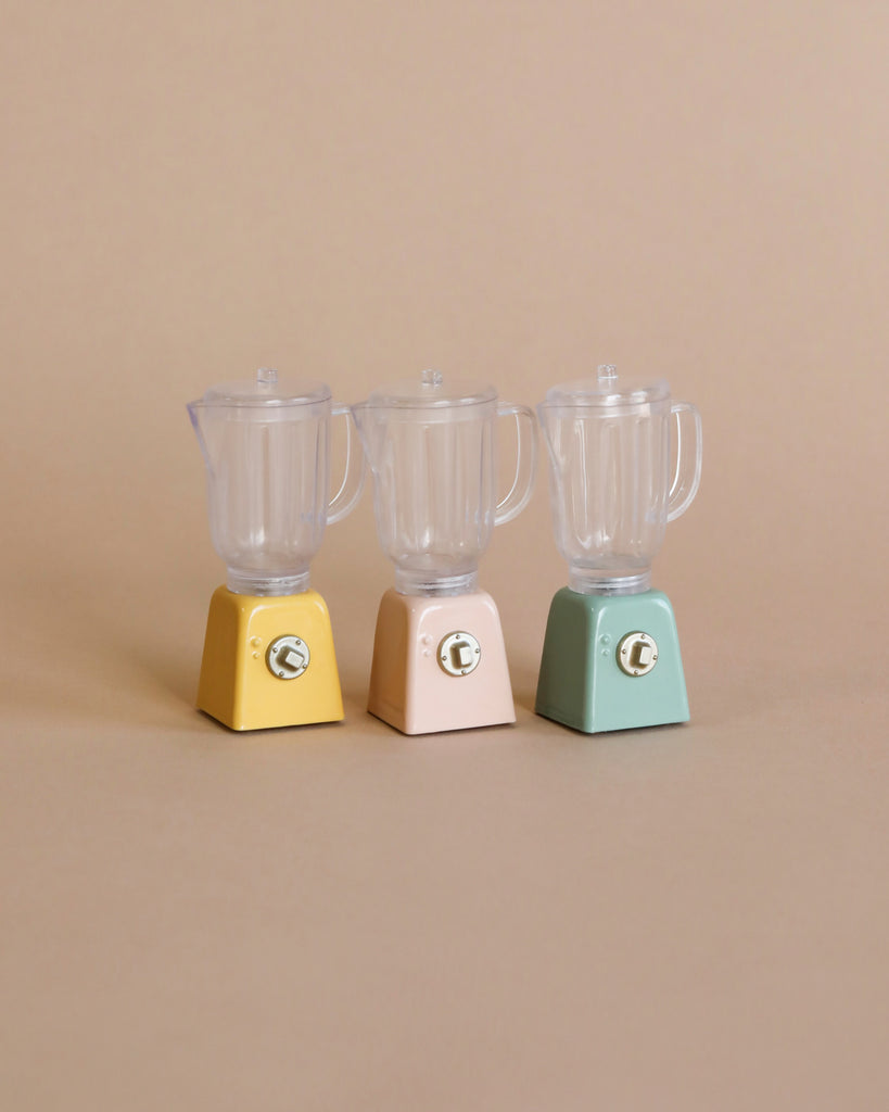 Three Maileg Miniature Blender models are displayed side by side on a beige background. The first miniature blender is yellow, the second is pink, and the third is green. Each children's toy has a clear, empty container on top and a simple control knob on the front—perfect for pretend play.