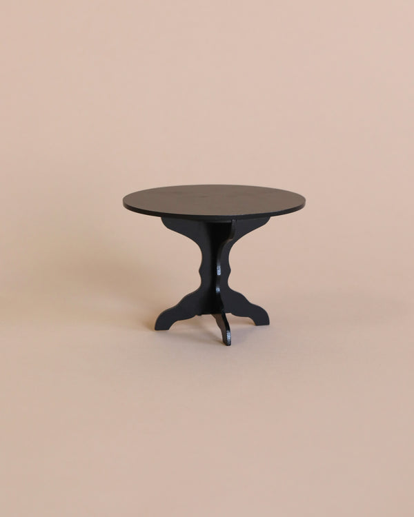 A small, anthracite Maileg Miniature Coffee Table with a three-legged base stands against a plain, light beige background. The design is simple and minimalist, making it perfect for a contemporary Maileg dollhouse setup.