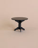 A small, anthracite Maileg Miniature Coffee Table with a three-legged base stands against a plain, light beige background. The design is simple and minimalist, making it perfect for a contemporary Maileg dollhouse setup.