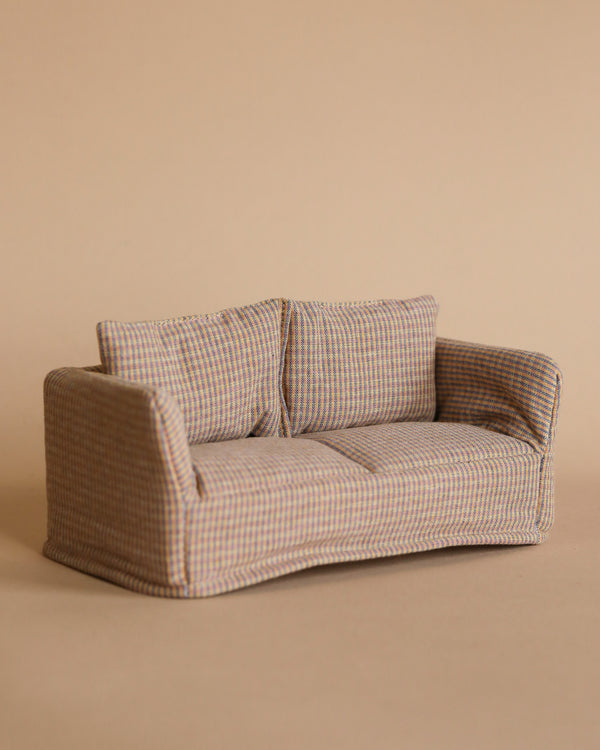 The Maileg Mouse Couch, a soft sofa with a fabric-covered checkered pattern, sits against a plain beige background. This loveseat features two cushions and armrests, offering a cozy and inviting appearance ideal for any Mouse Hole Farmhouse.