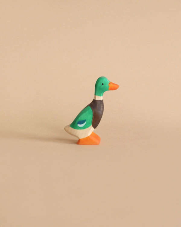 A Holztiger Mallard featuring a green head, brown neck, and orange beak stands on a plain beige background. The handcrafted wood duck has vibrant colors and is crafted in a simple, minimalist style, reminiscent of HOLZTIGER figures made in Europe.