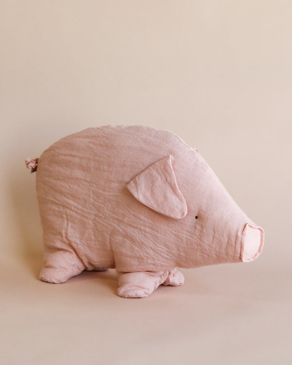 A soft, pink fabric pig toy named Maileg Large Polly Pork stands on a light beige background. This cute pig has simple, sewn features including small black eyes, a snout, and floppy ears. Its texture appears slightly wrinkled, adding a handmade charm to this adorable stuffed animal.